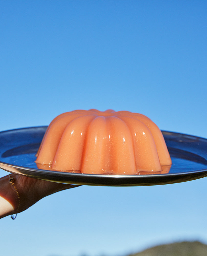 Hand holidng Guava Nectar Gelée in bundt form on a silver platter against a clear blue sky