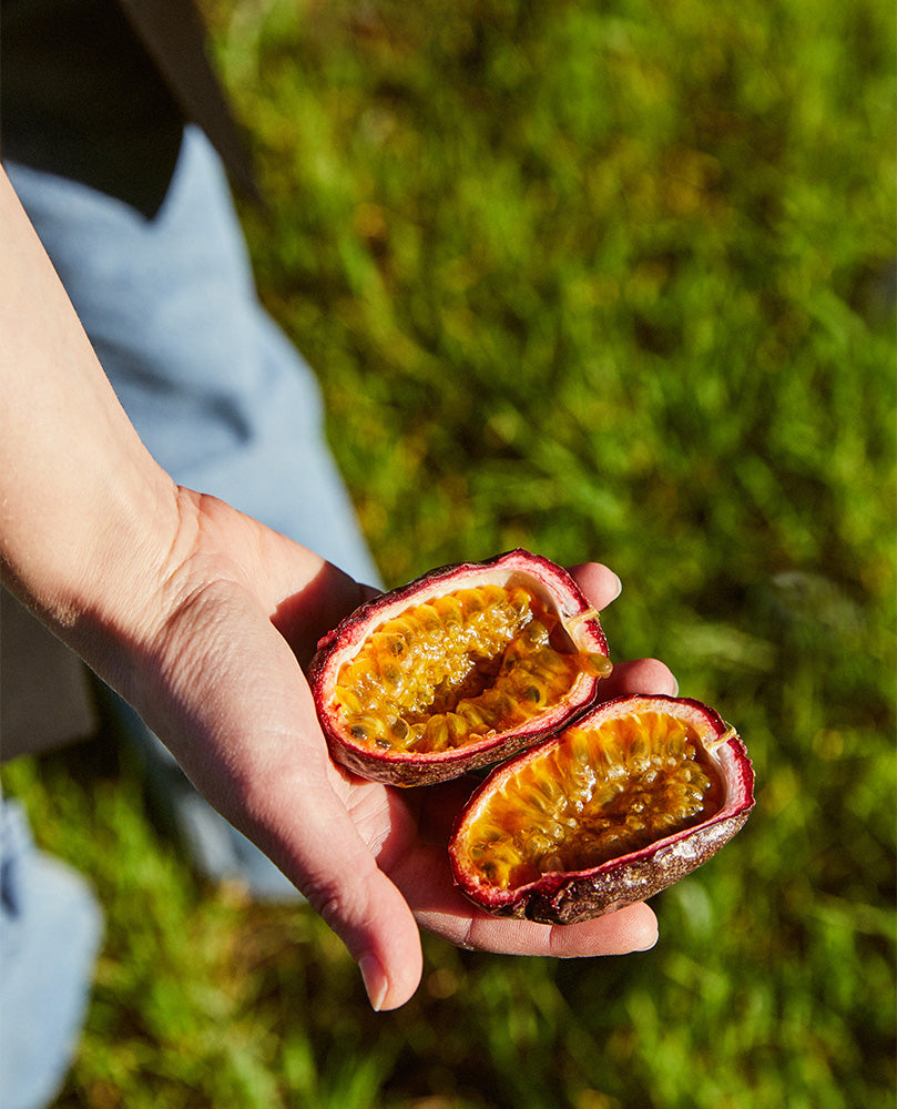 Hand holding two halves of passion fruit on grassy background