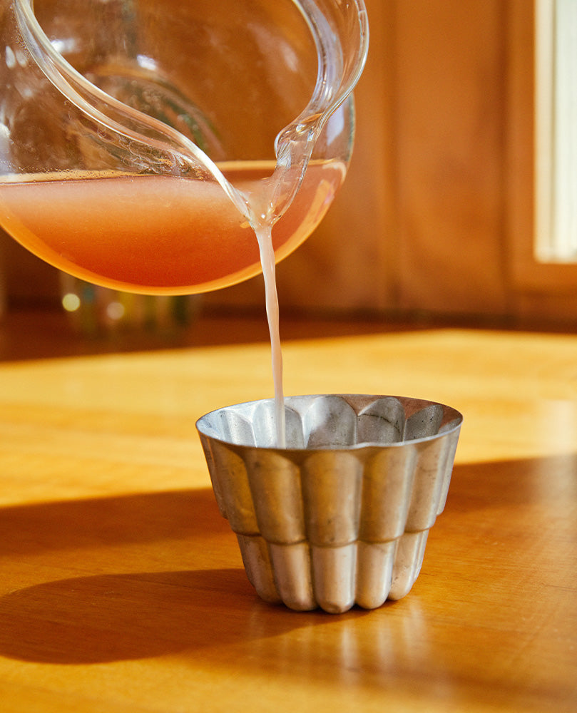 Pitcher pouring liquid gelatin into small silver mold