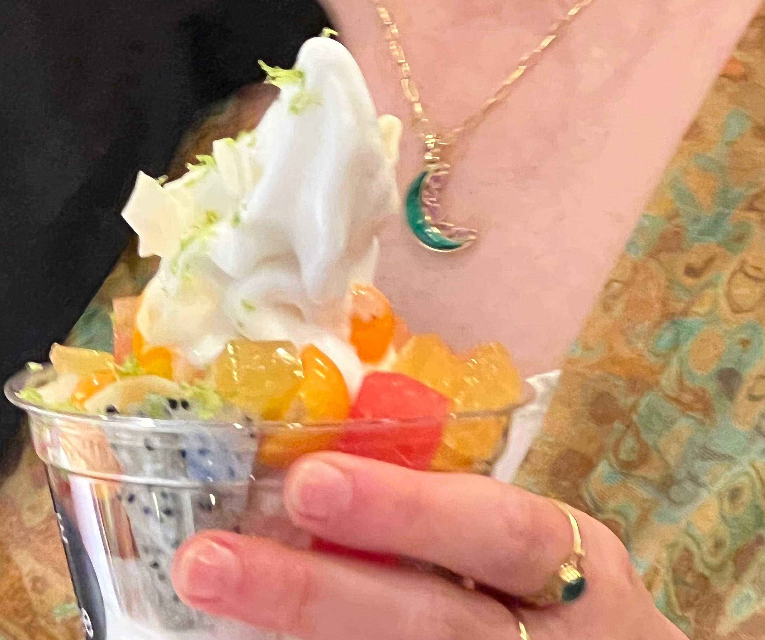 Person holding a cup of fruit and jellies with soft serve topping