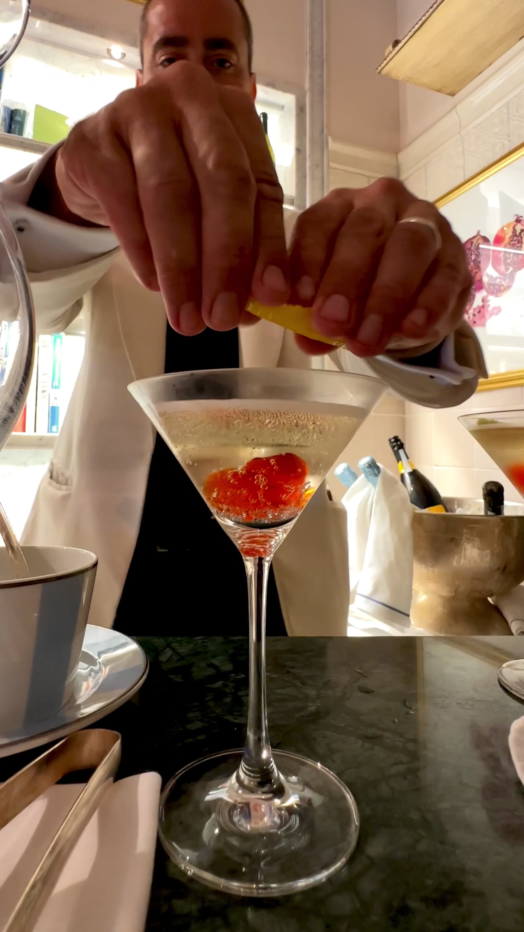 Main in white suit making a martini with jellies and lemon peel